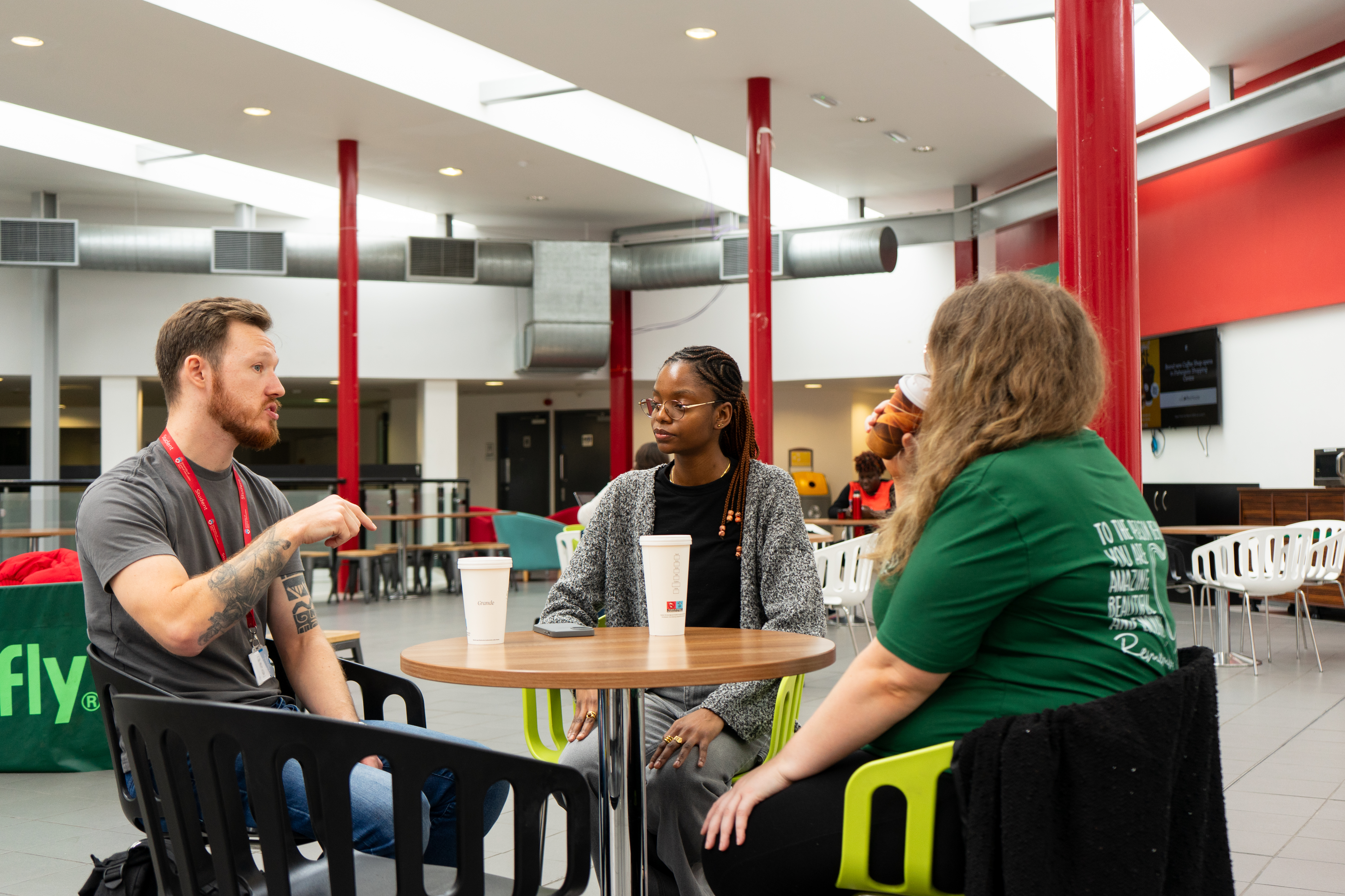 3 students sat talking around a table in the Student's Union Cafe space